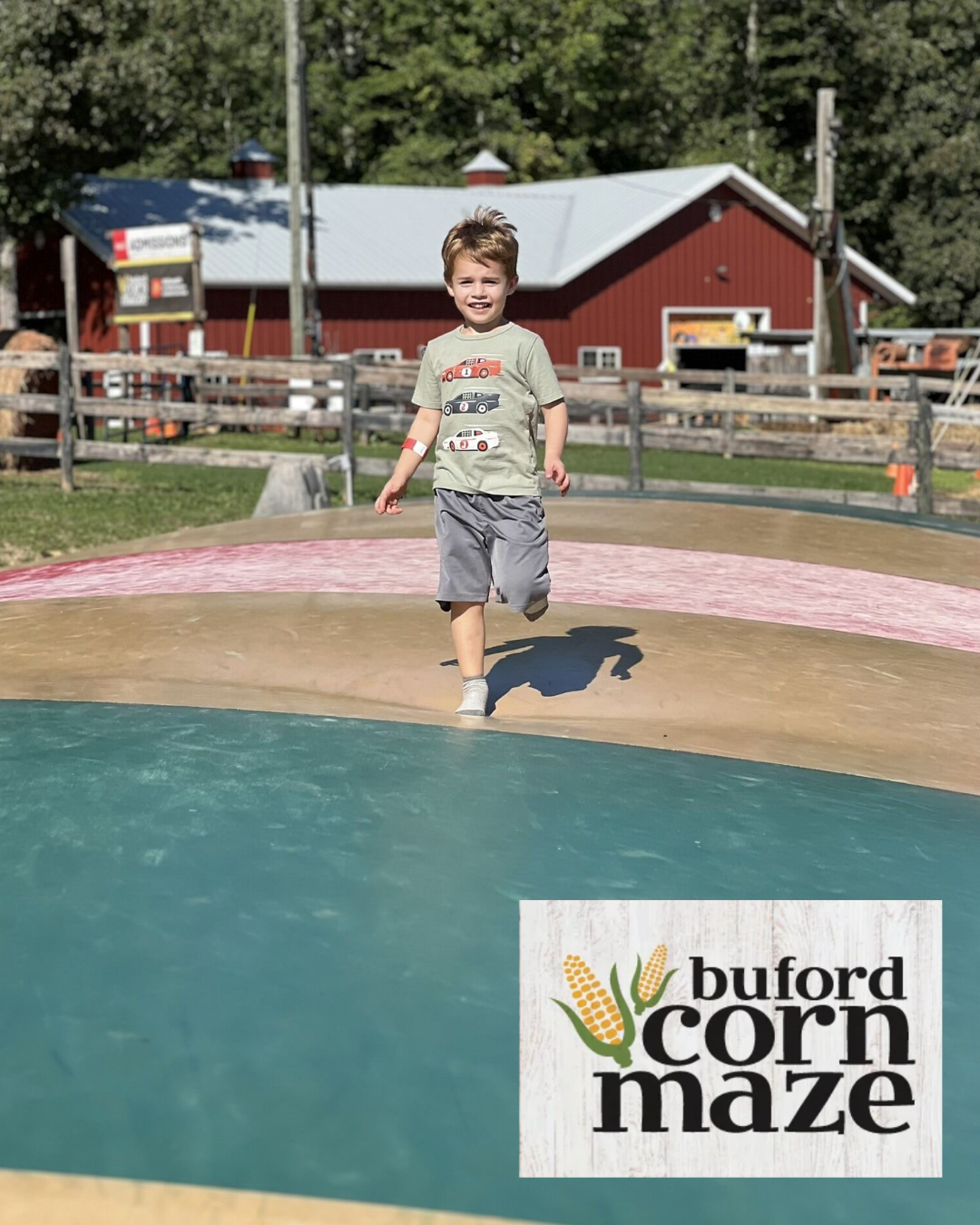 Boy runs toward camera on a teal play area at Buford Corn Maze, red barn in background.