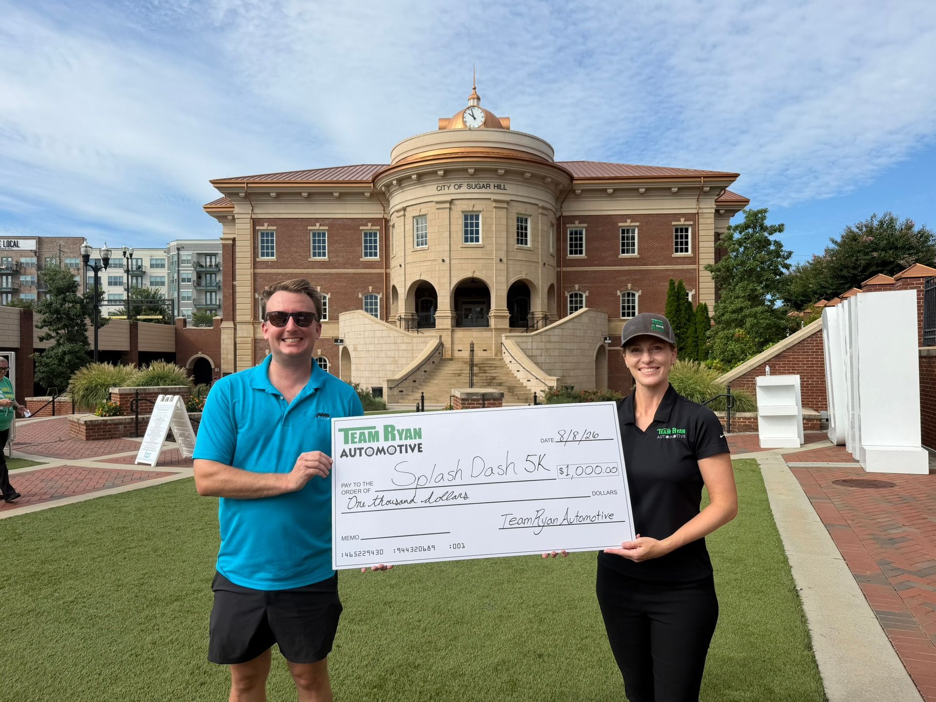 Shara from Team Ryan Automotive presents a $1,000 sponsorship check to Chris of AMS Pools in front o