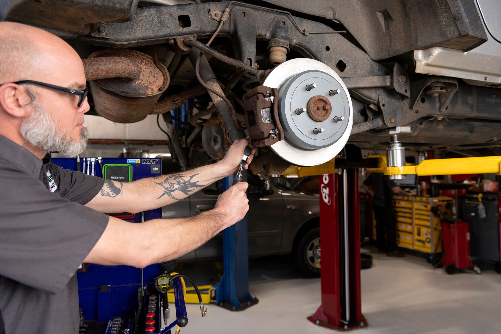 Mechanic inspecting a car’s front brake rotor on a lift in an auto shop