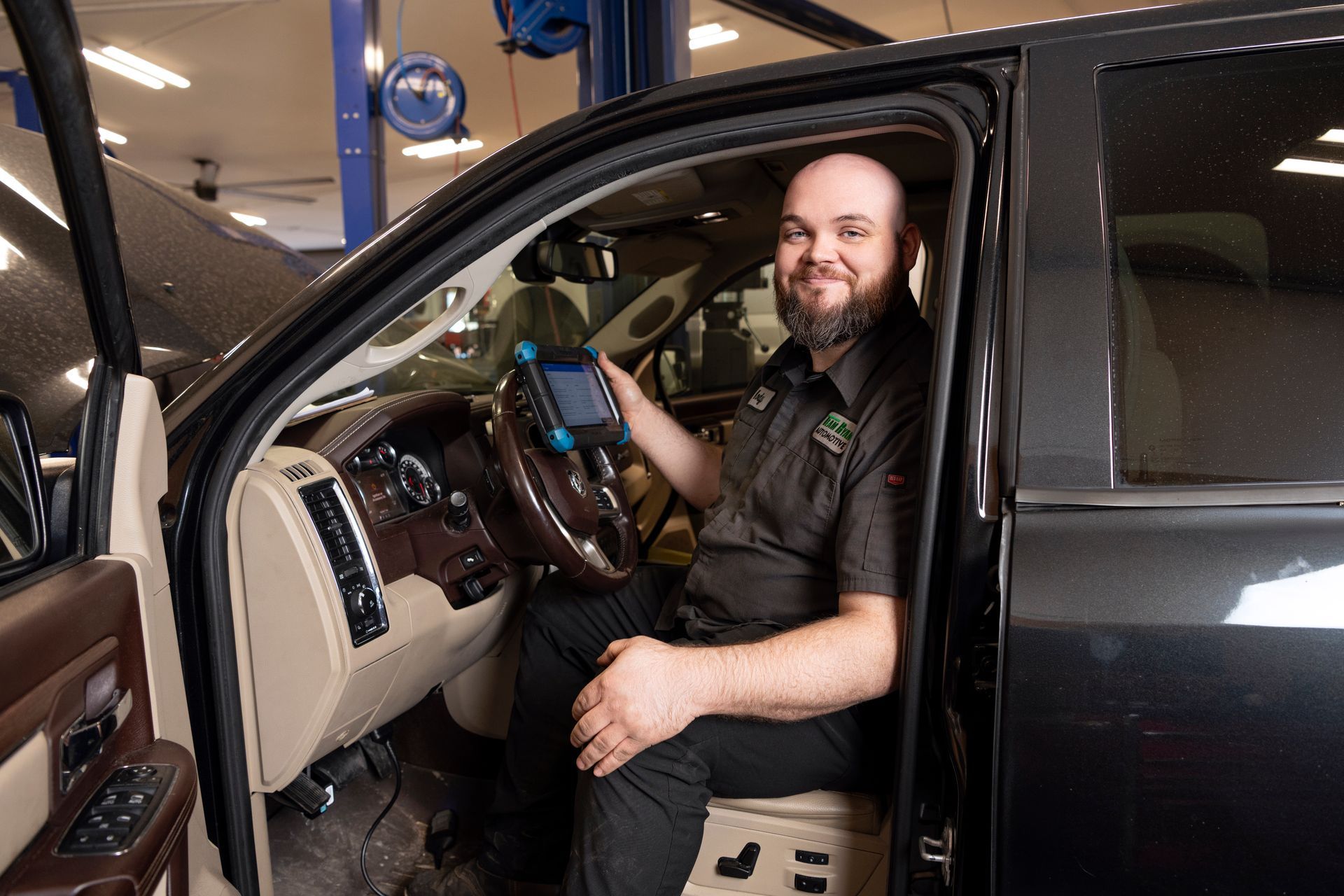 Bearded man sitting in the driver’s seat of a black SUV, holding a phone and smiling.