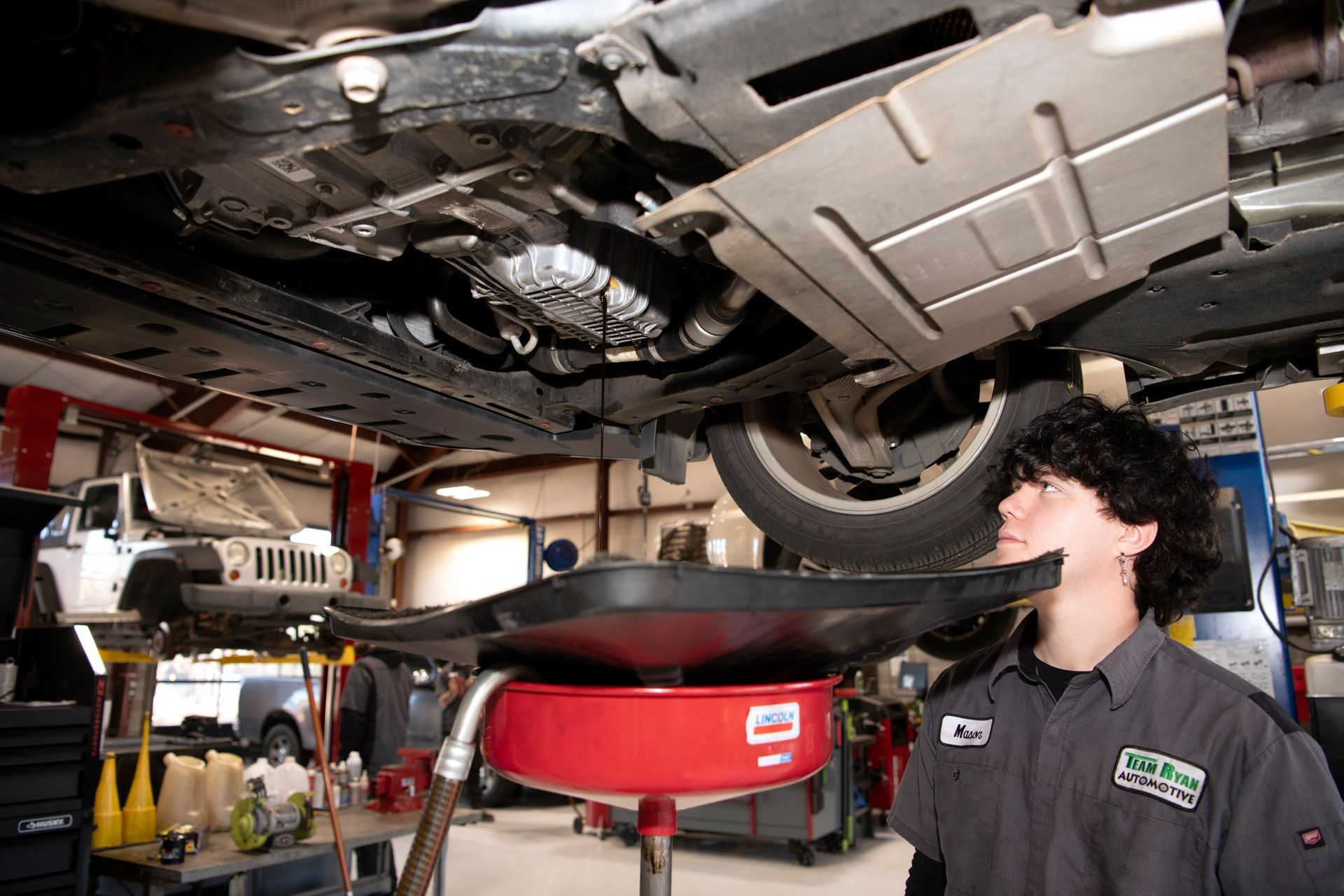 Mechanic inspecting the underside of a car on a lift in an auto repair shop