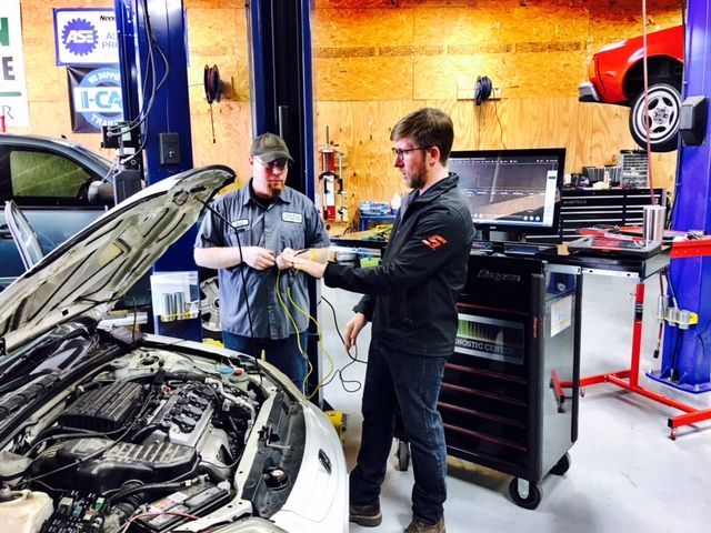 Two mechanics inspecting an open car hood in an auto repair shop