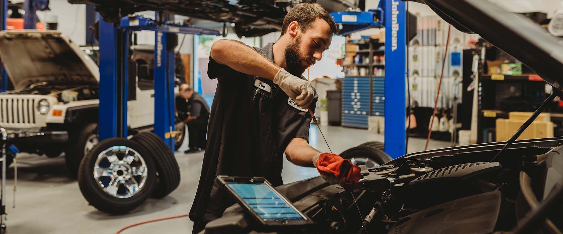 Mechanic repairing a car engine in an auto shop, using a red tool beside a laptop