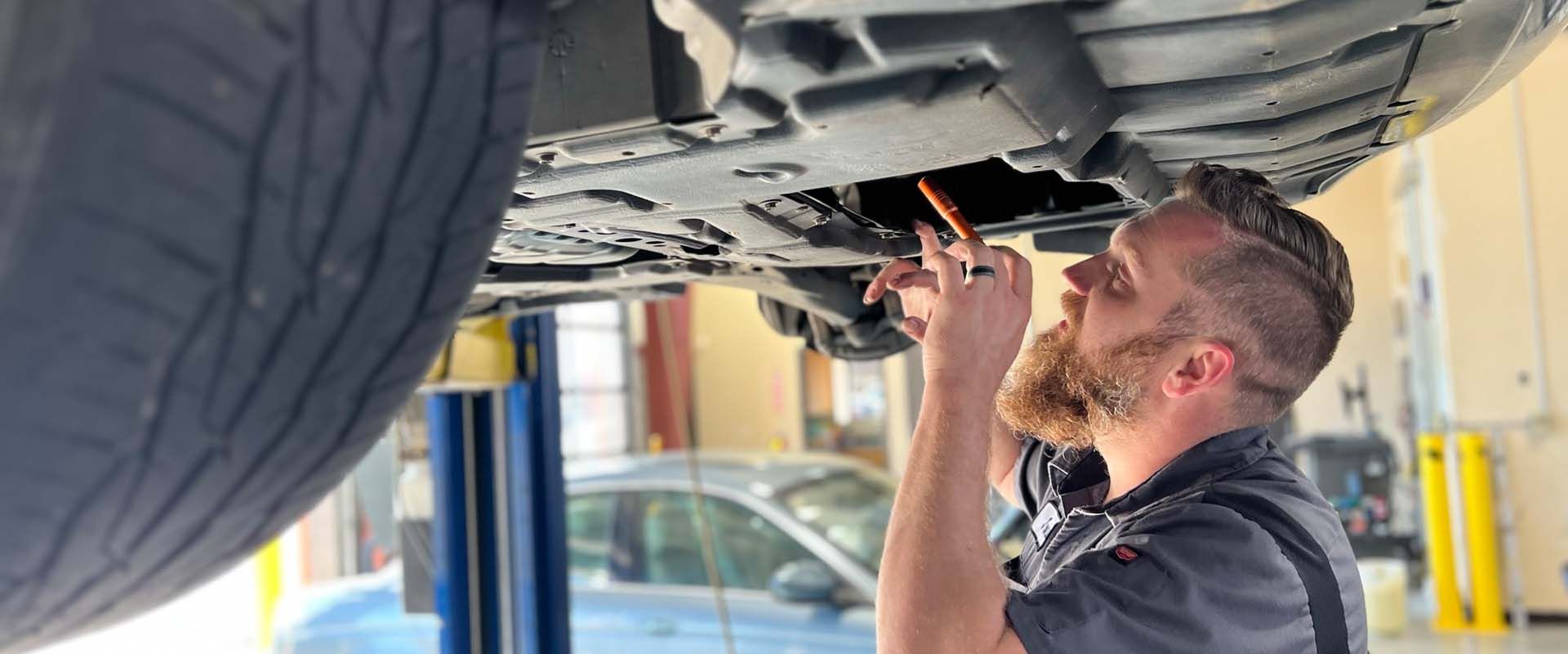 Mechanic inspecting a vehicle’s underside with a tool in an auto shop