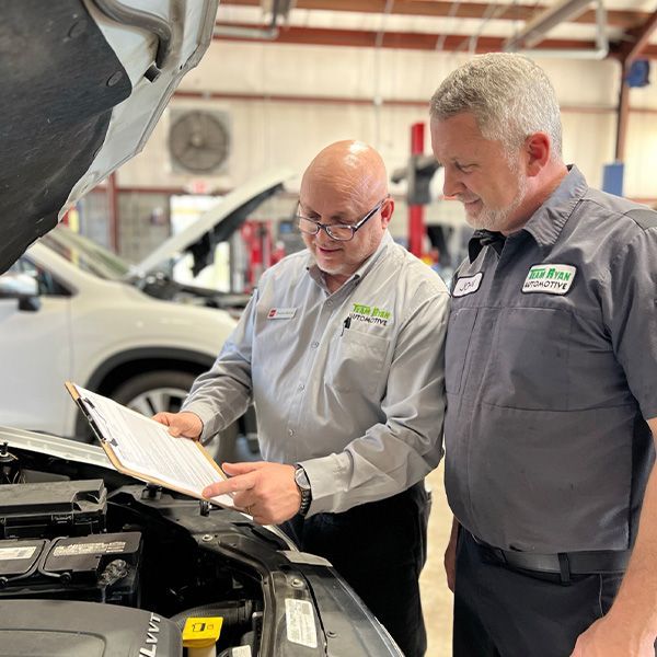 two men are looking under the hood of a car