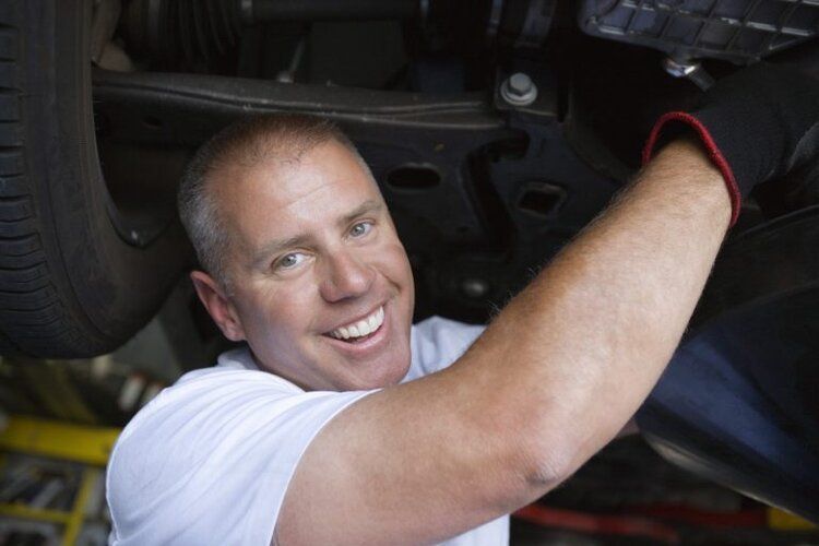 a man is working under a car in a garage and smiling .