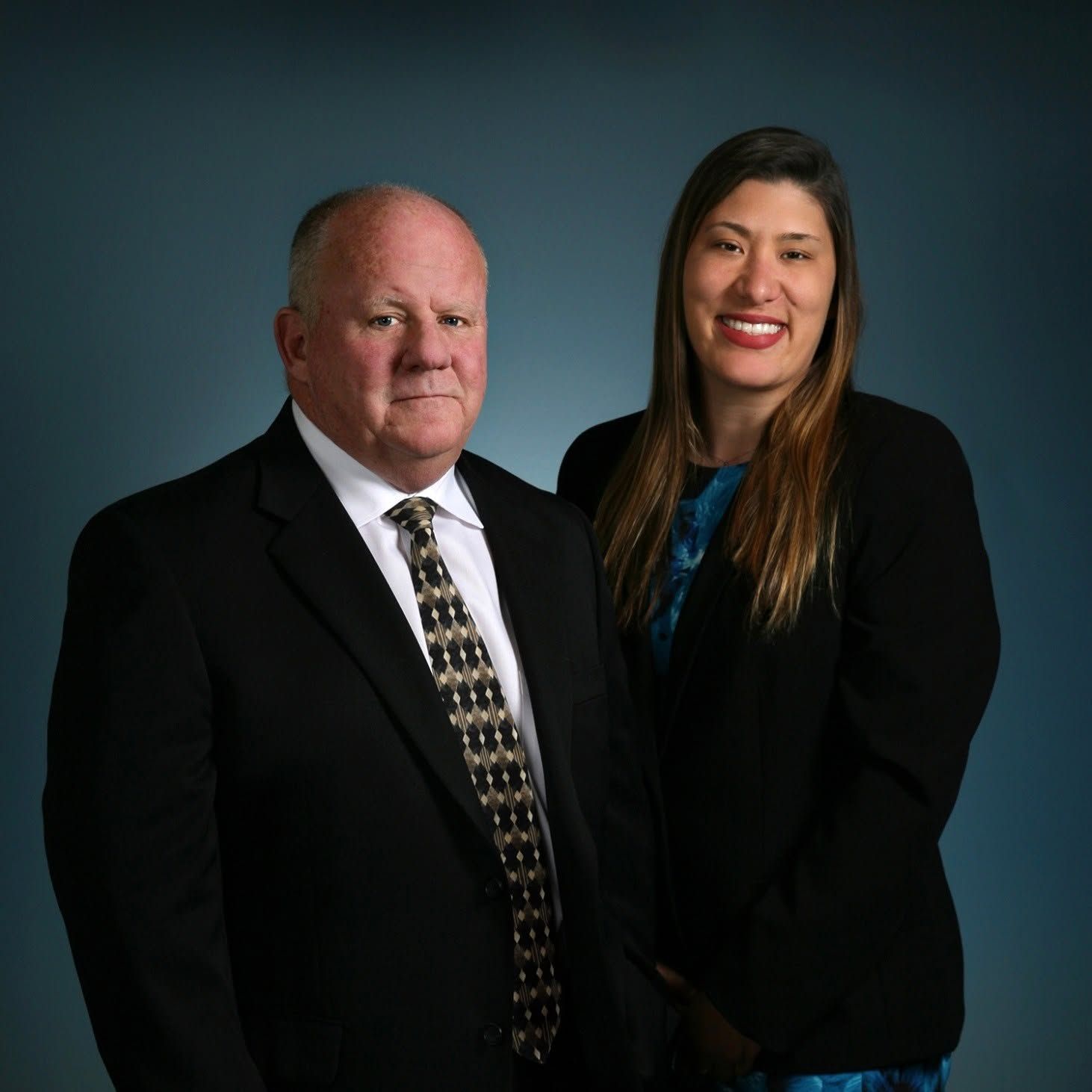 Two professionals posing in business attire against a dark studio backdrop