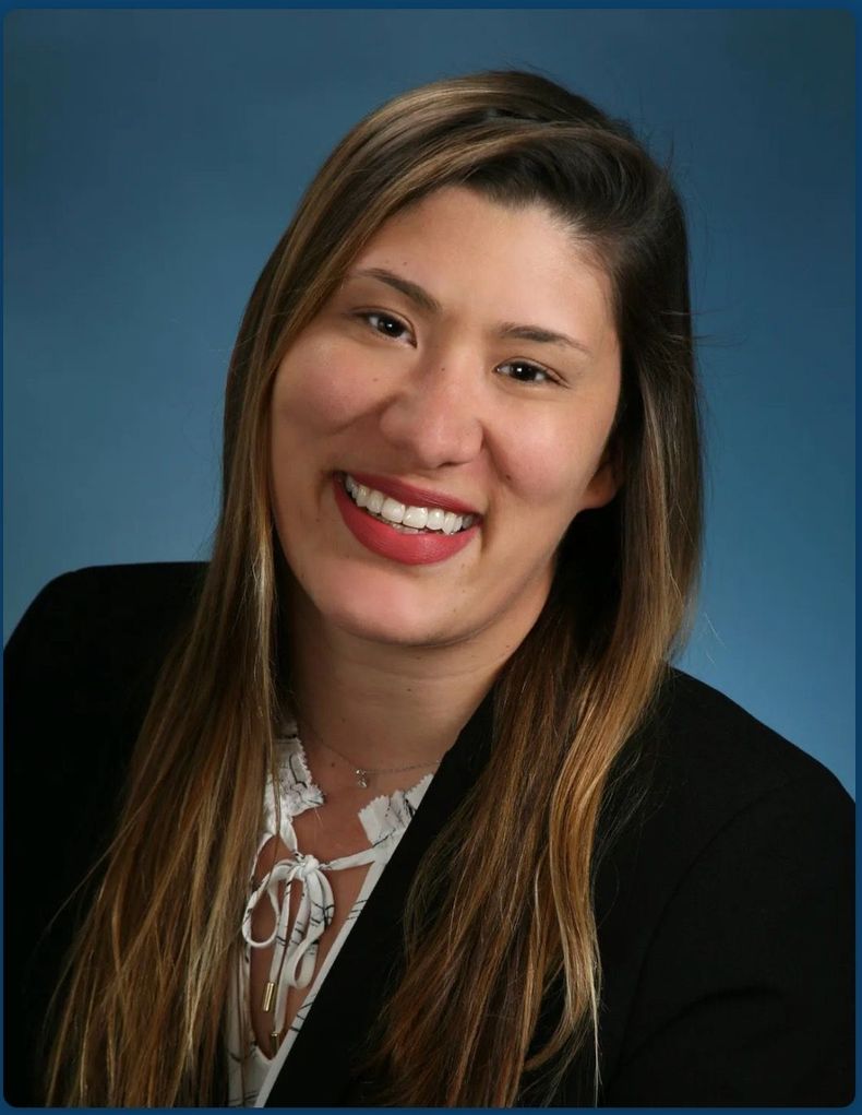 Smiling woman in a black blazer against a blue studio backdrop