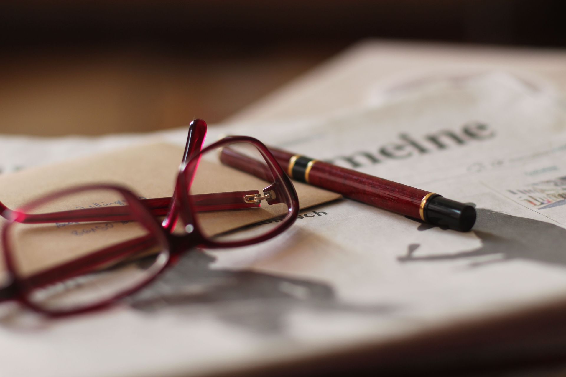 Red glasses and a pen resting on a newspaper page.