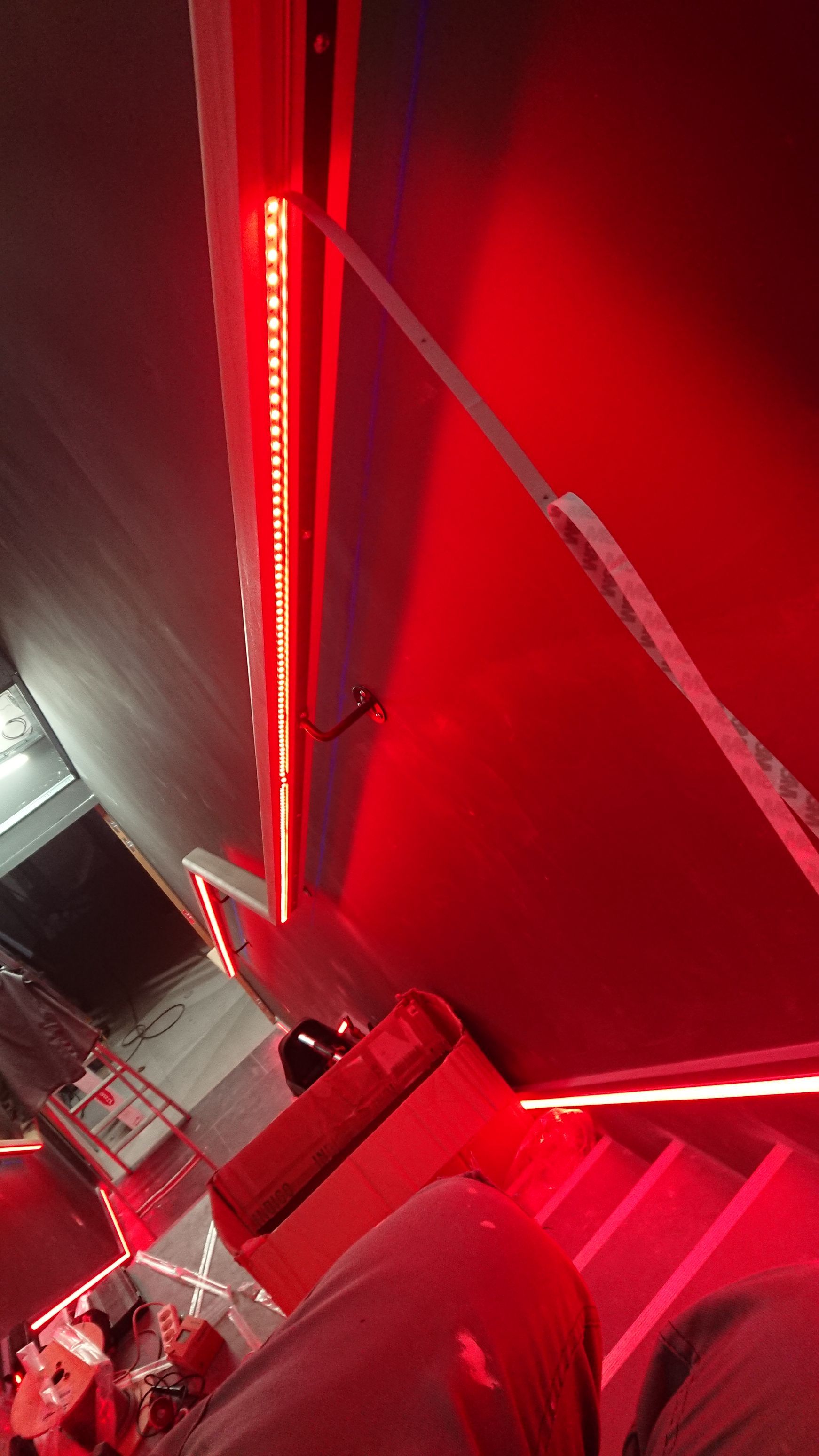 Une personne se tient dans une pièce avec des lumières rouges sur les murs et les escaliers.