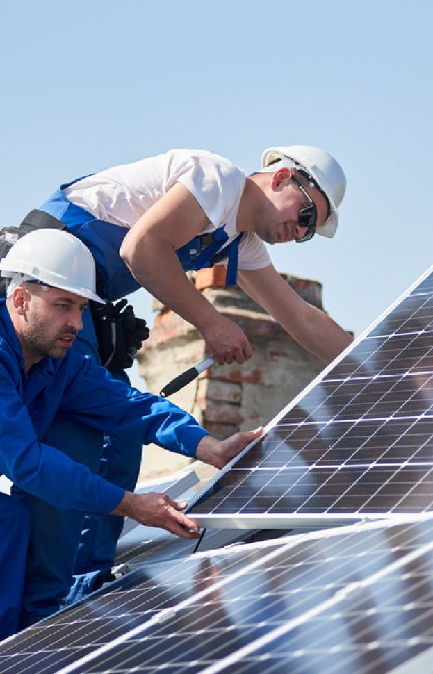 Workers installing solar panels on a rooftop under a clear blue sky