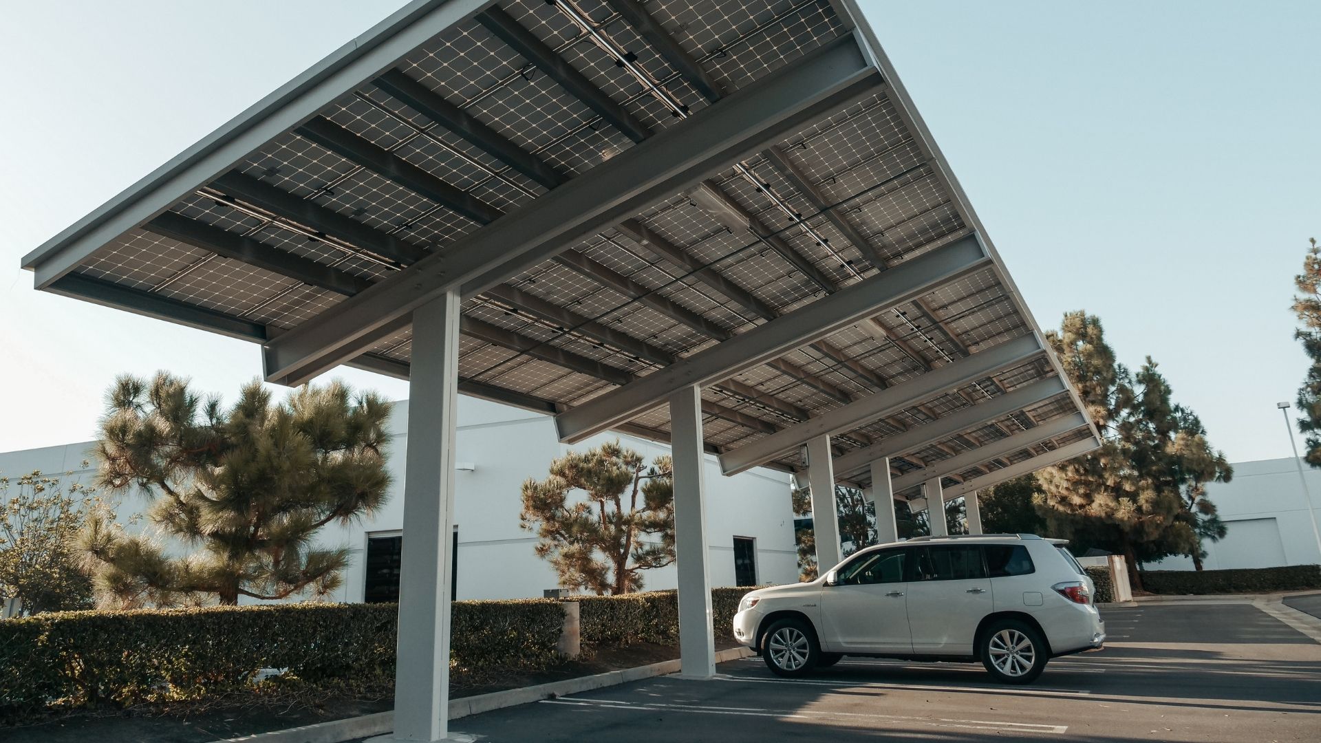 Solar-panel carport shading a parked white SUV in a parking lot under clear skies.