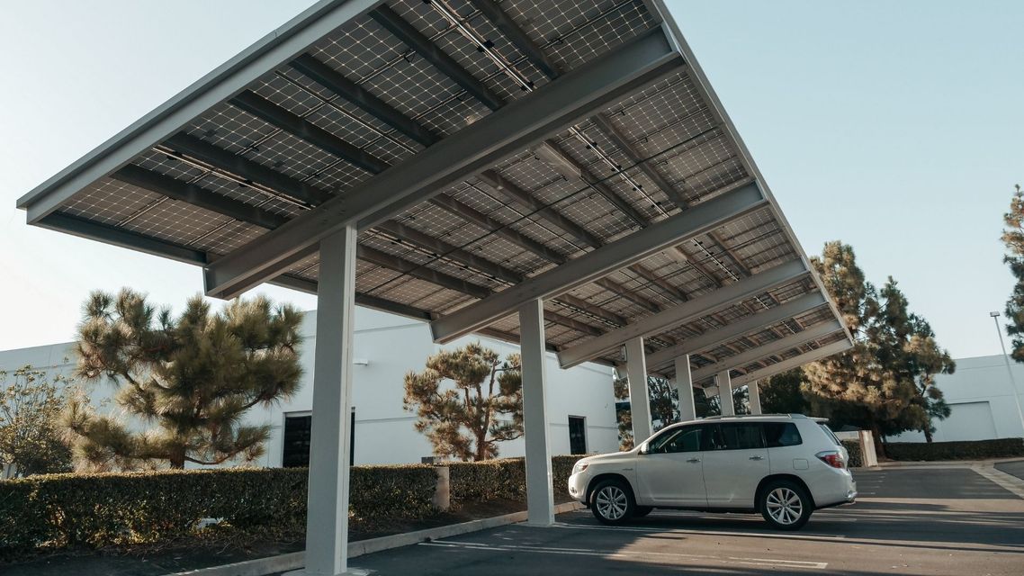 Solar-panel carport shading a parked white SUV in a parking lot under clear skies.