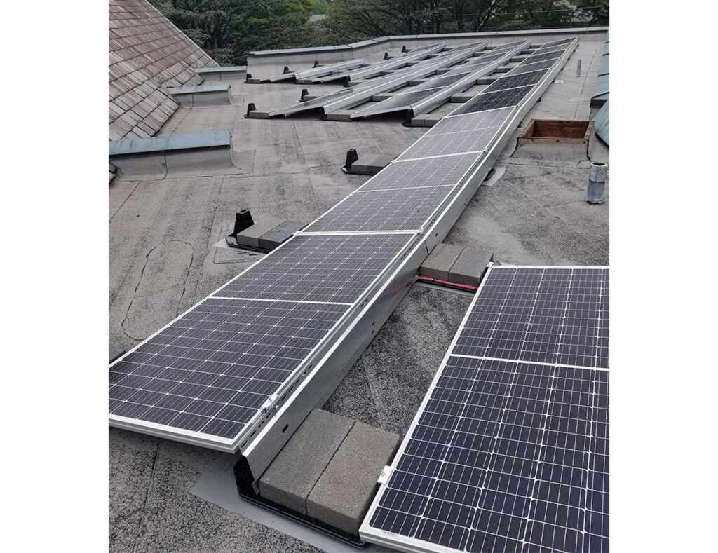 Rows of solar panels on a rooftop, with a central raised walkway and surrounding gravel surface