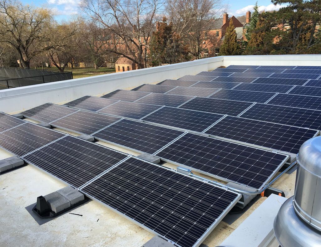 Solar panels installed on a white rooftop with trees and houses in the background.