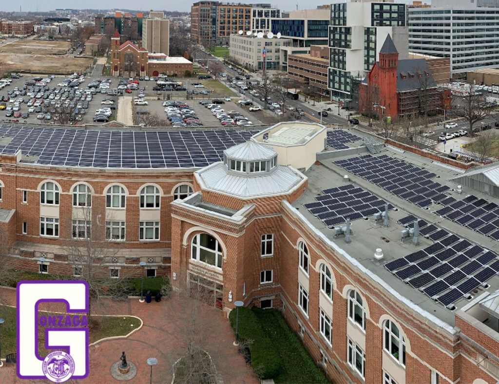 Aerial view of brick campus buildings with solar-panel rooftops and a large parking lot