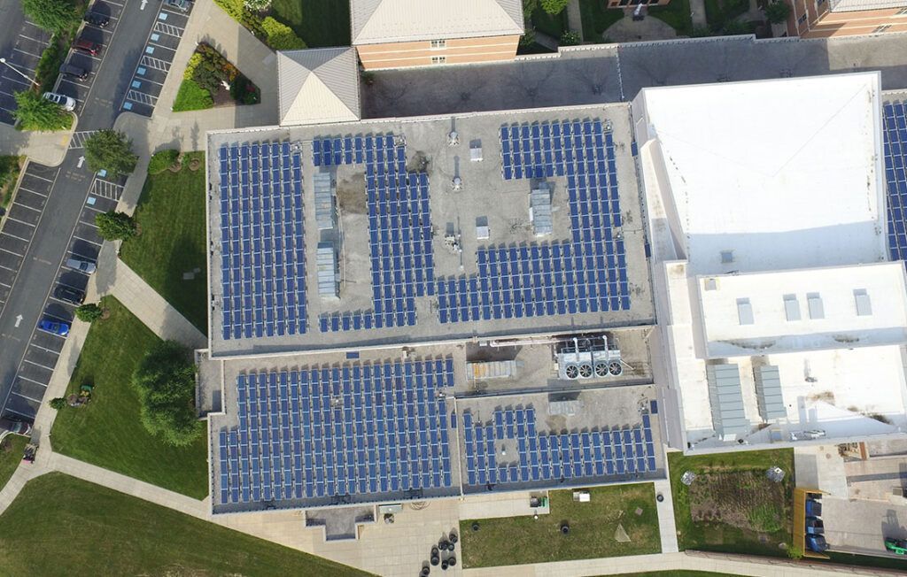 Aerial view of solar panels covering rooftops in a large parking lot beside buildings and trees