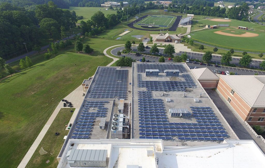 Aerial view of a building roof covered with solar panels beside a baseball field and green lawns