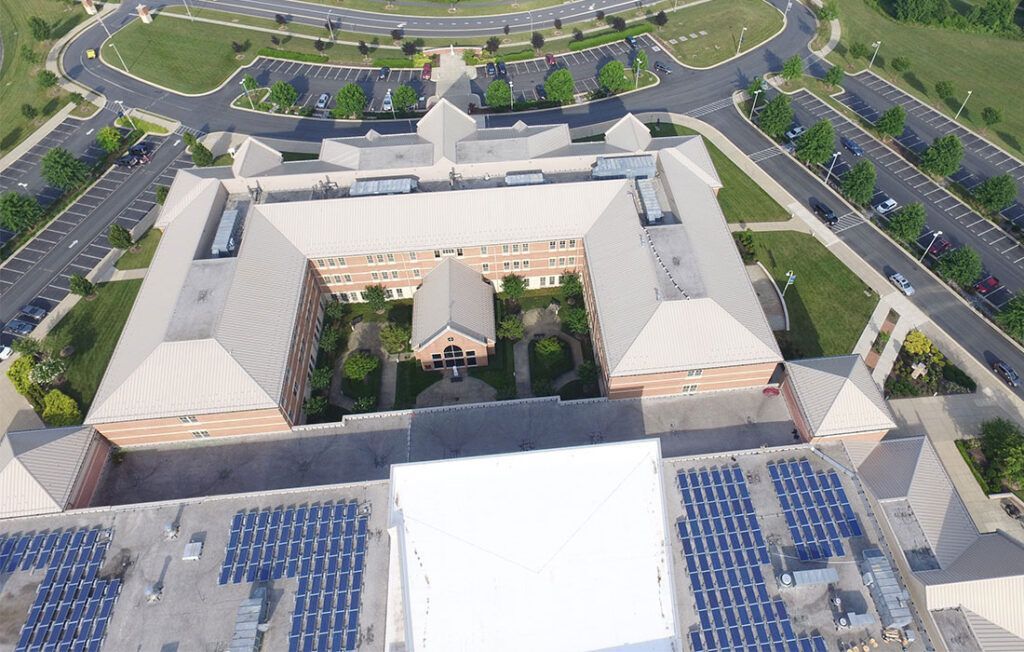 Aerial view of a large white building complex with parking lots and landscaped roads around it.
