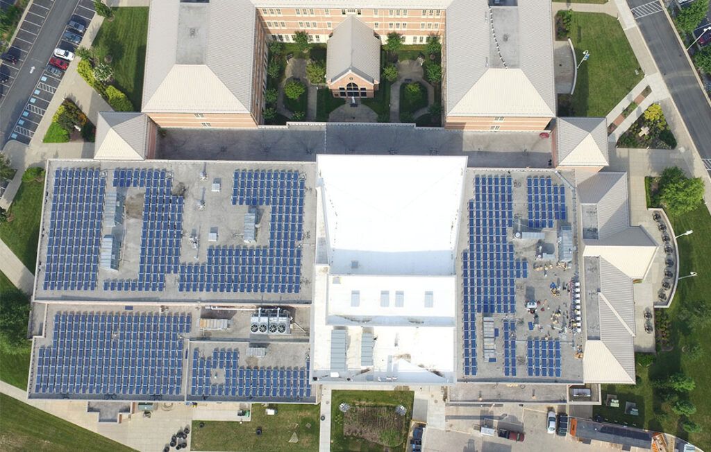 Aerial view of a rooftop with rows of blue solar panels and a large white tent in the center