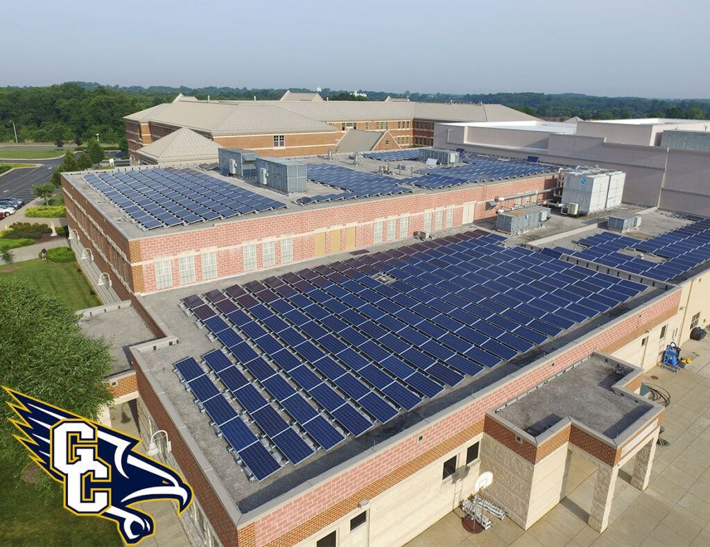Aerial view of a school building with blue solar panels on the roof and a logo in the corner