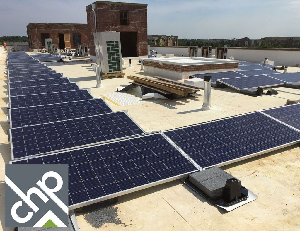Rooftop solar panel array with a small brick building and picnic tables on a sunny day