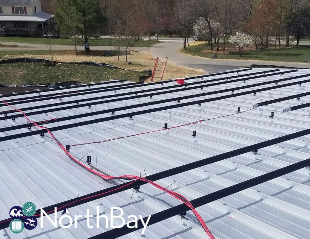 Roof under construction with gray panels, black rails, and red safety lines on a building site