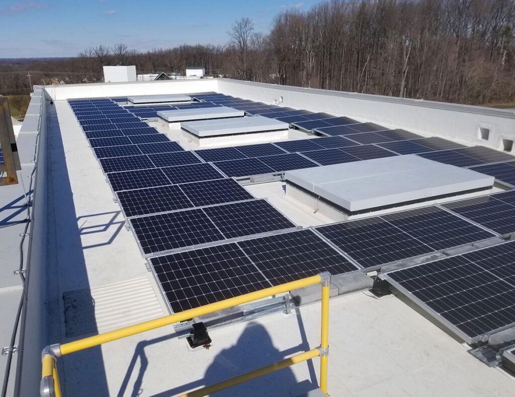 Rooftop solar panel array on a flat white building under a clear sky.