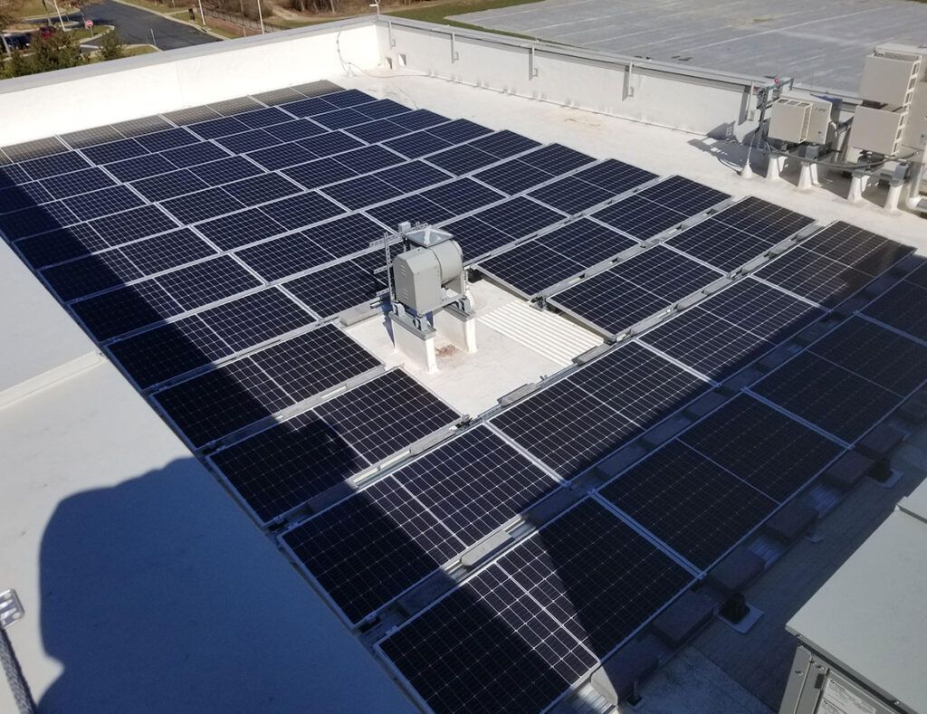 Rooftop solar panel array on a flat industrial roof, with HVAC units and bright sunlight.