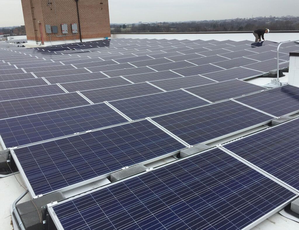 Rooftop solar panels arranged in rows beside a brick building under a cloudy sky.