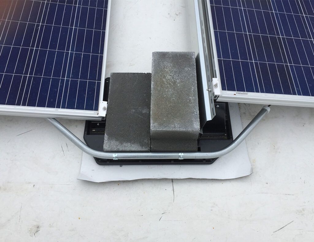 Solar panels with a metal rooftop mount and white cable conduit on a white surface.