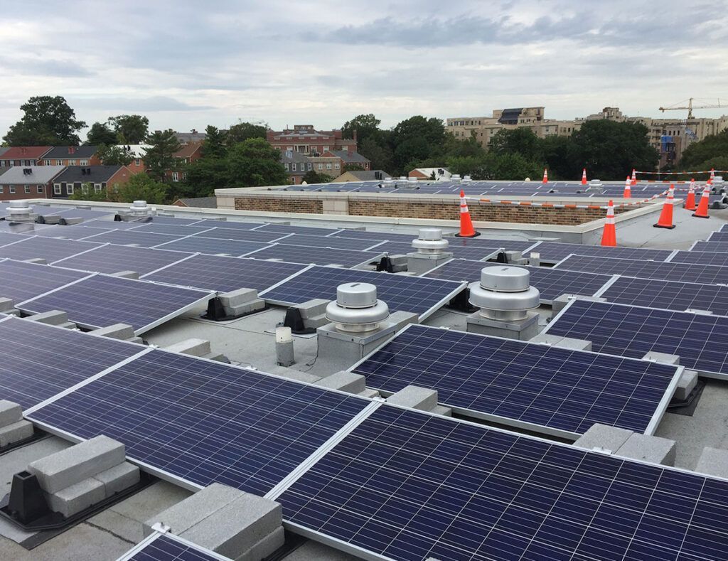 Solar panels on a rooftop with orange safety cones and city buildings in the background