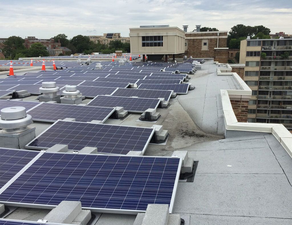 Rooftop with rows of blue solar panels on a flat white roof in an urban area