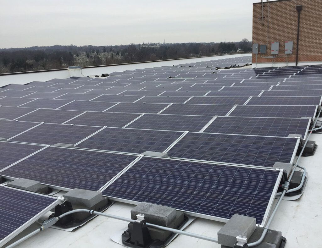 Snow-covered rooftop with rows of solar panels beside a brick building