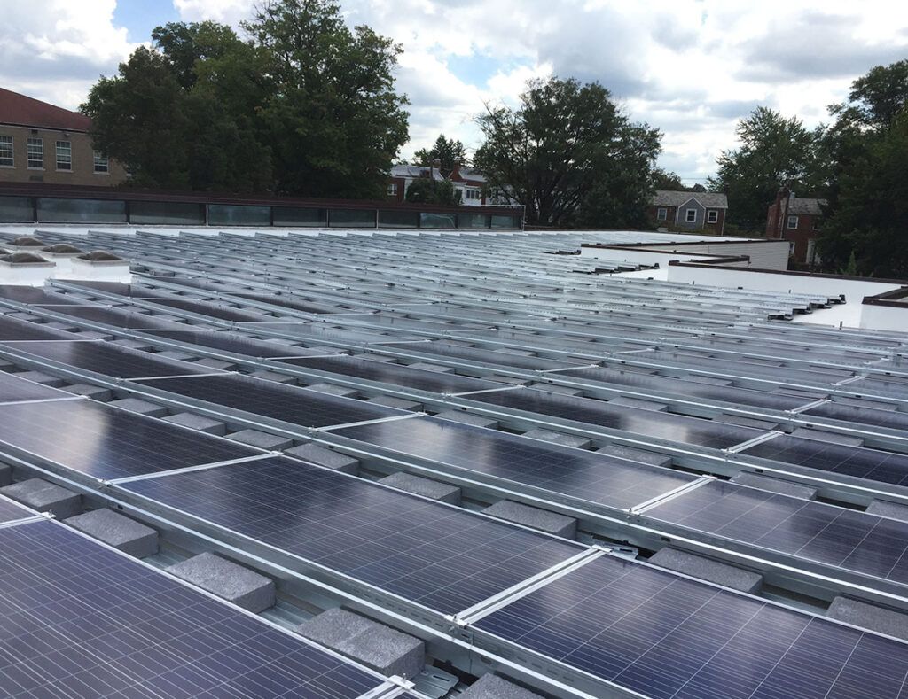 Solar panels covering a rooftop under a cloudy sky, with trees and buildings in the background