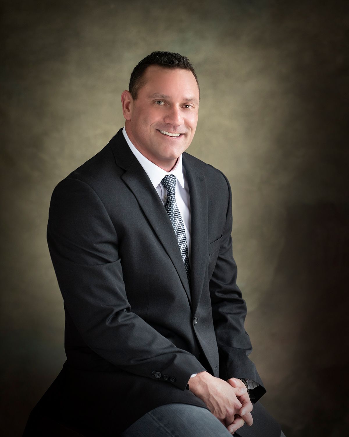 A man in a suit and tie is sitting with his hands folded