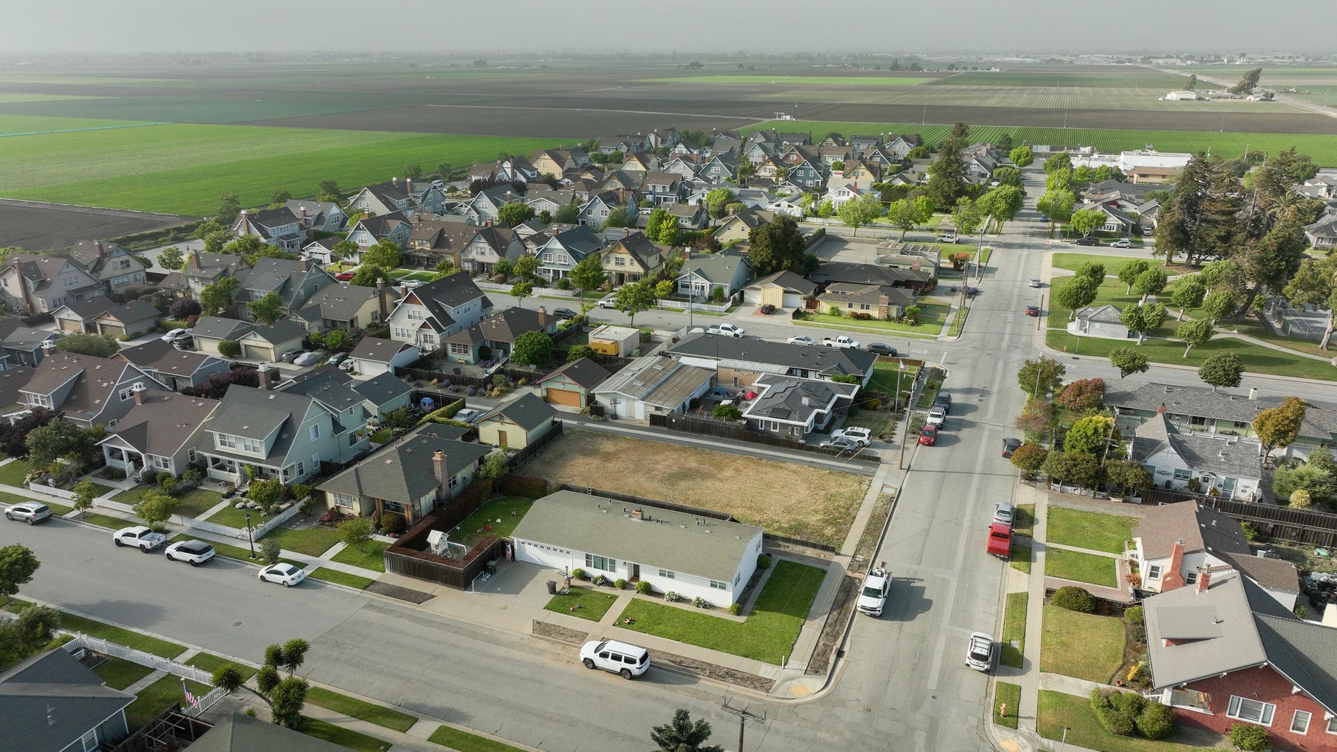 Aerial view of a suburban neighborhood with houses, streets, and fields in the background.