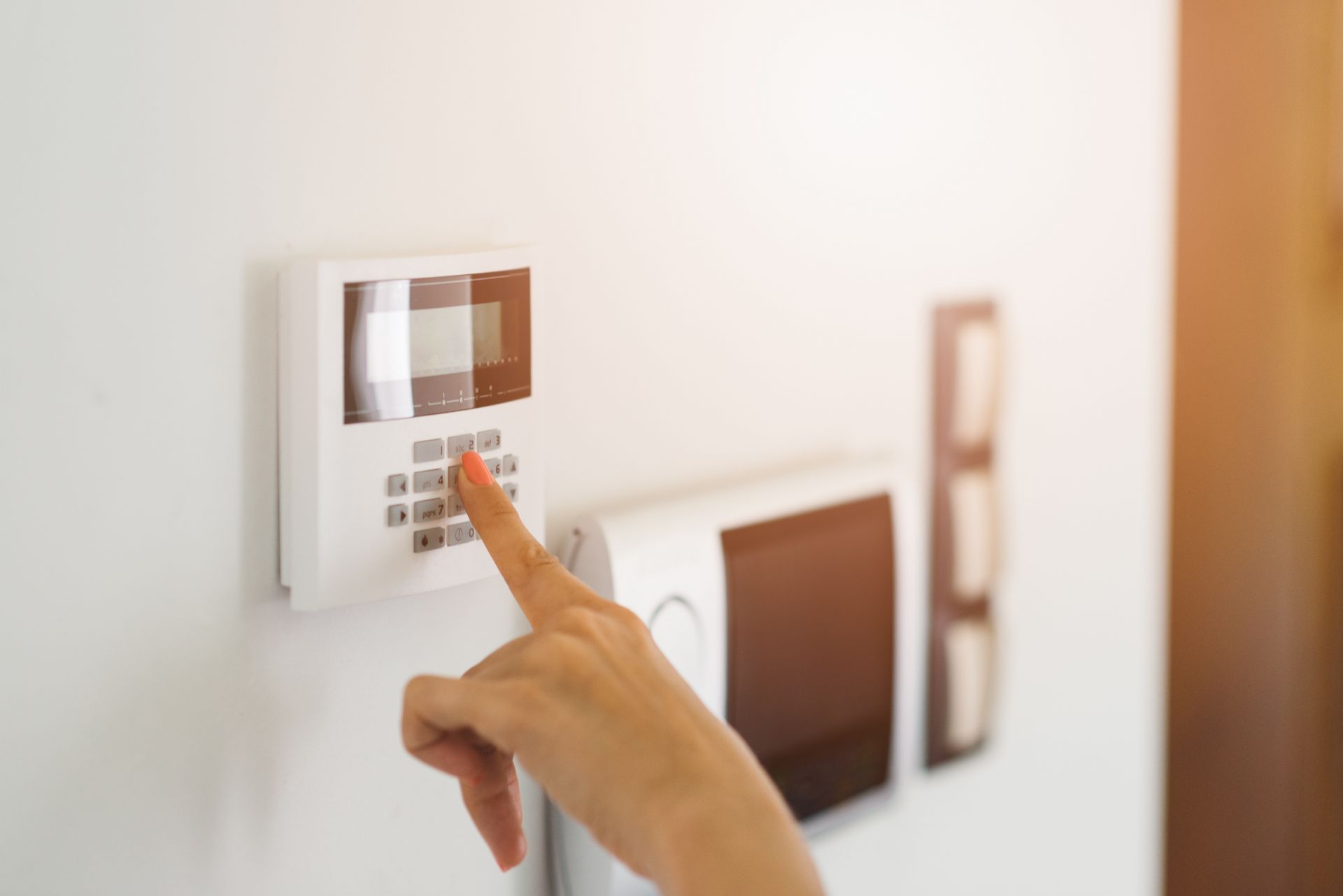Hand pressing a button on a white security system keypad on a white wall. Hand pressing a button on a white security system keypad on a white wall.