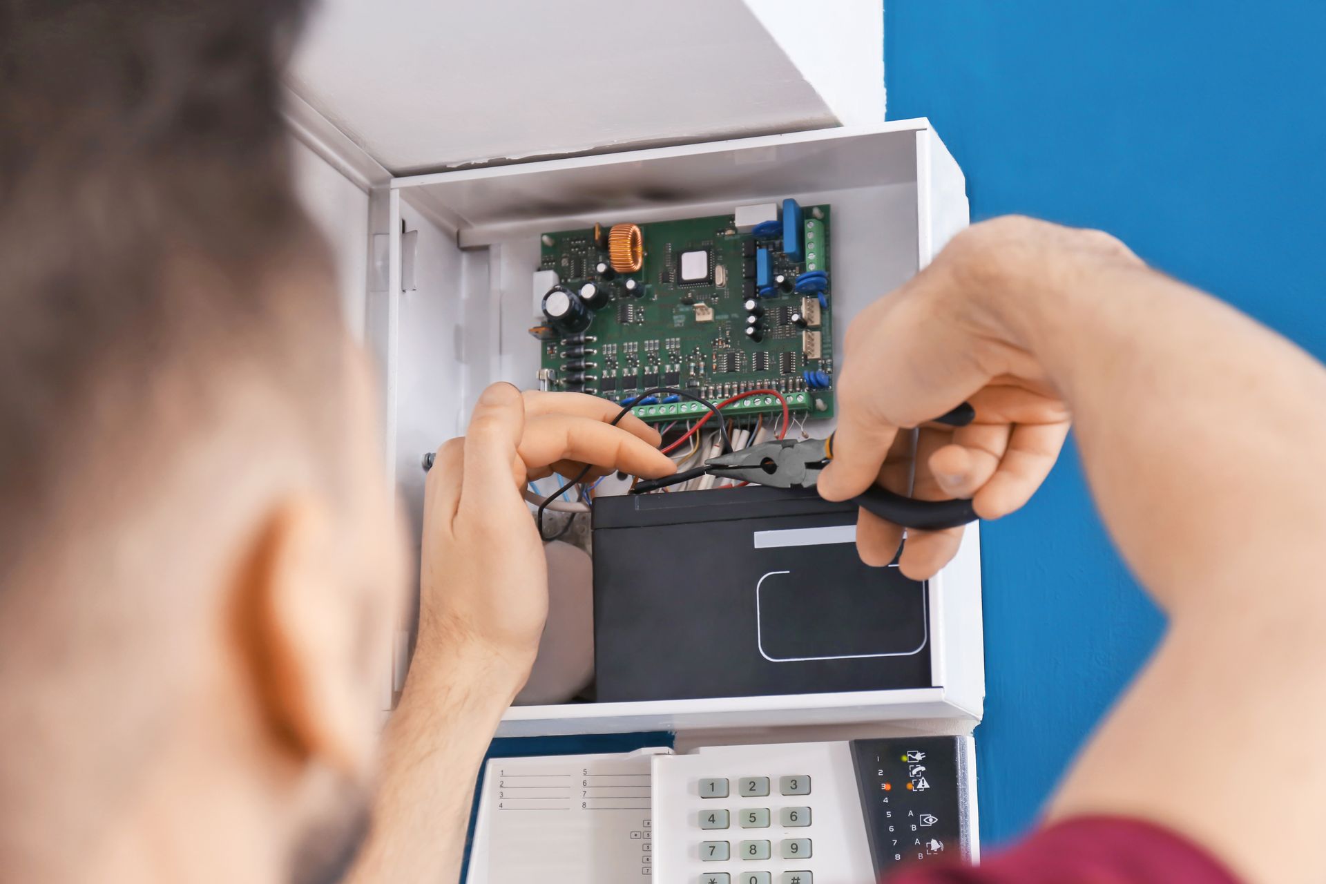 Person working on security system panel, using tool to adjust wires.
