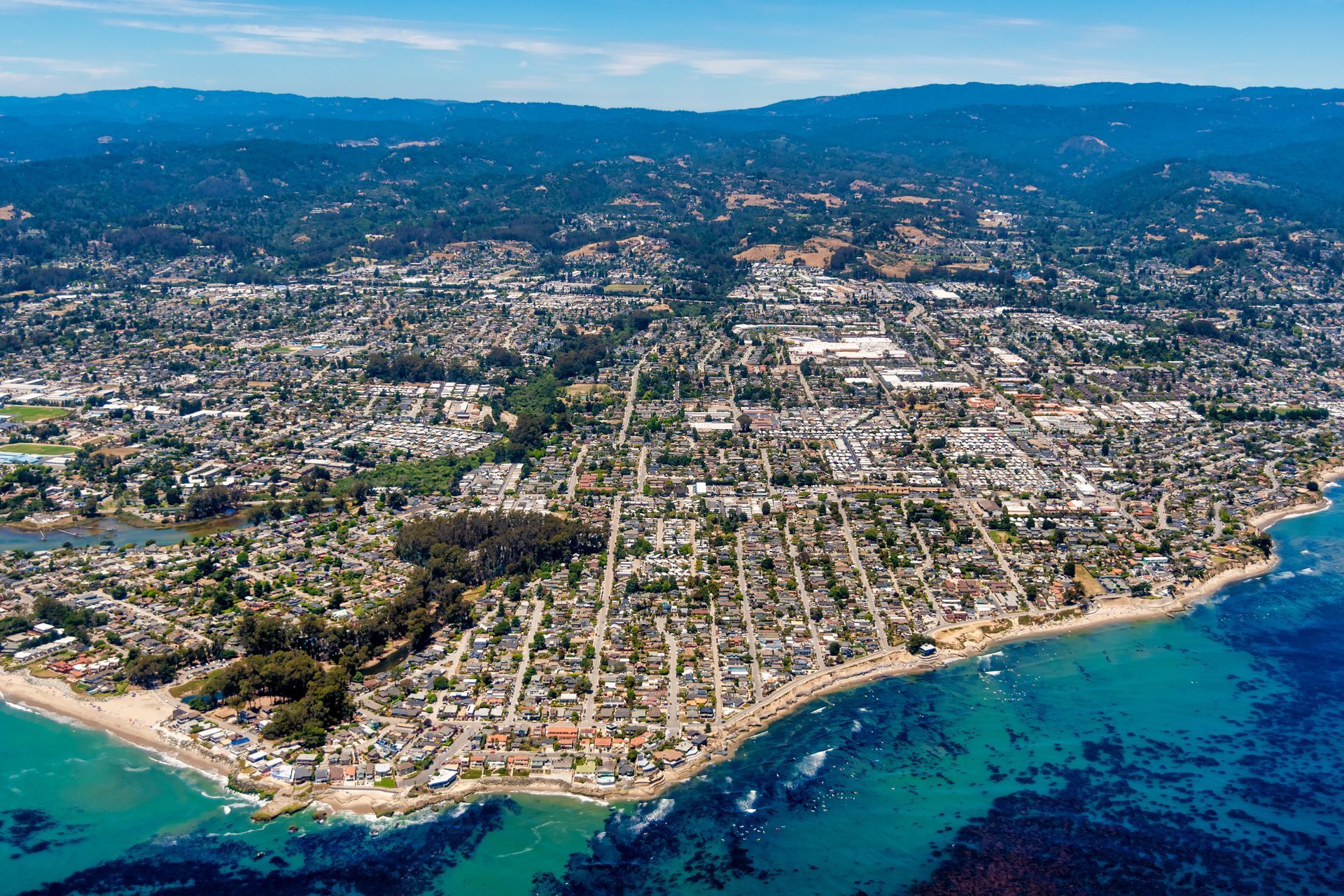 Aerial view of a coastal town with houses, roads, and a clear blue ocean under a sunny sky. Aerial view of a coastal town with houses, roads, and a clear blue ocean under a sunny sky.