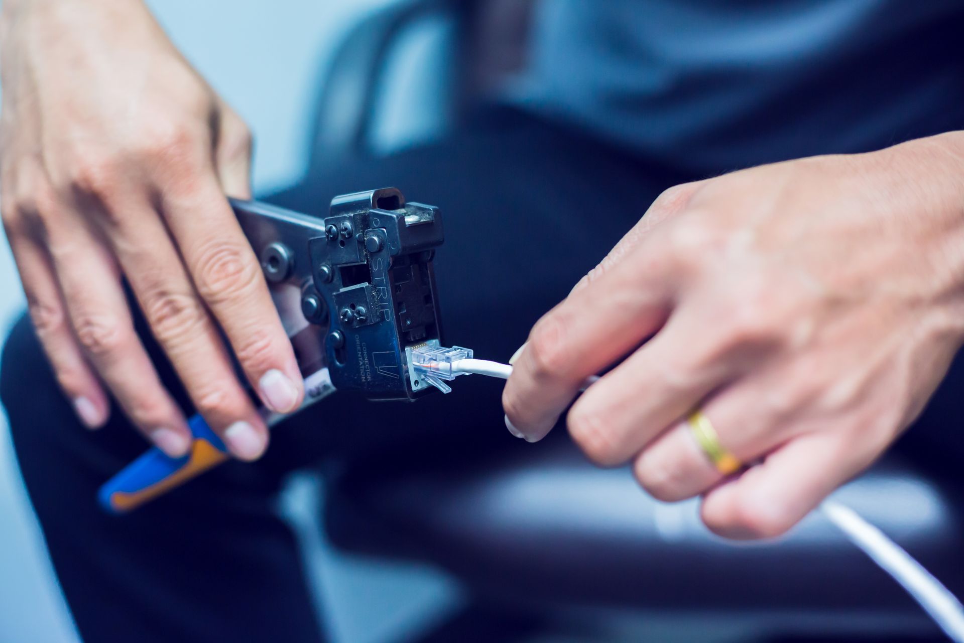 Hands crimping a network cable with a blue and gray crimping tool.