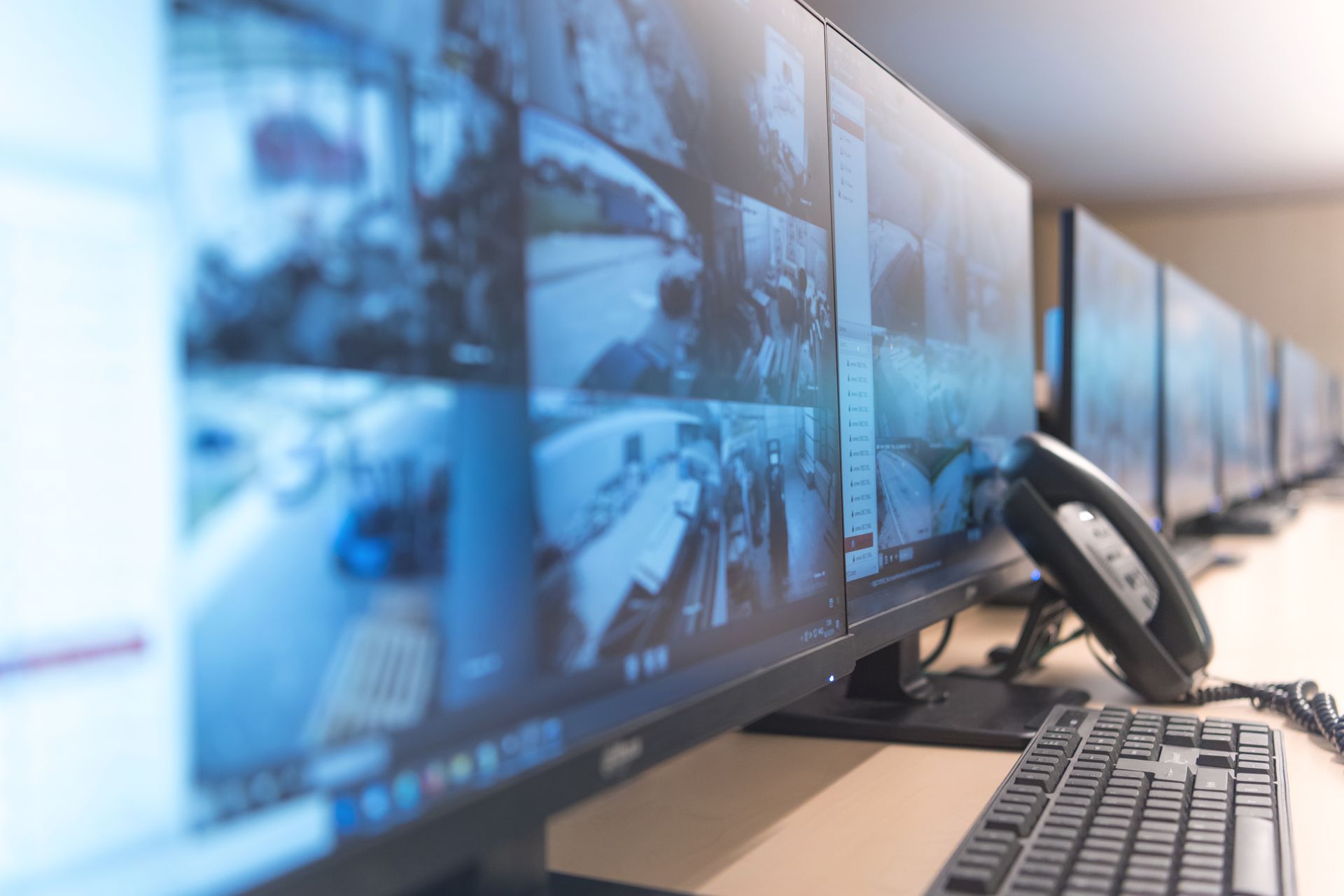 Security monitors displaying surveillance footage. A telephone and keyboard are in the foreground. Security monitors displaying surveillance footage. A telephone and keyboard are in the foreground.