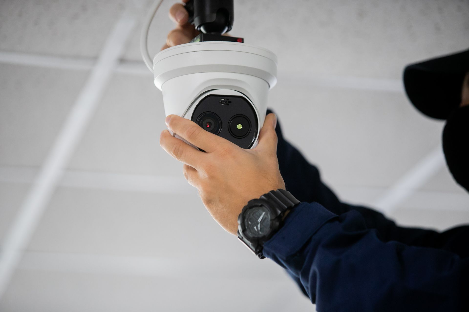 Person installing a white security camera on a white ceiling.