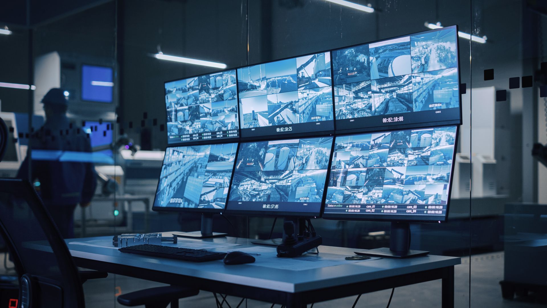 Monitors displaying security camera footage in a control room, with a person in the background. Monitors displaying security camera footage in a control room, with a person in the background.