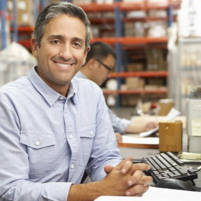 A man is sitting at a desk in front of a computer in a warehouse.