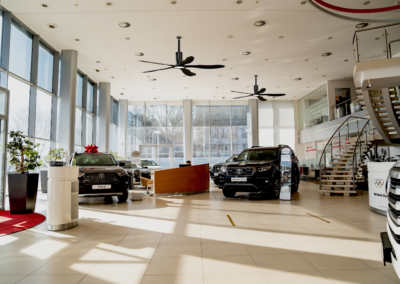 A car dealership with cars on display and ceiling fans.