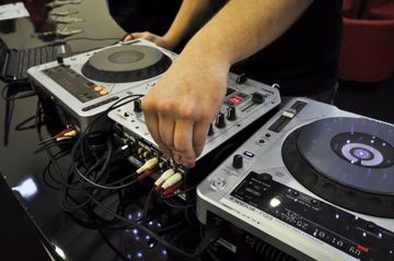 Hands adjusting controls on a DJ mixer between two turntables with glowing lights