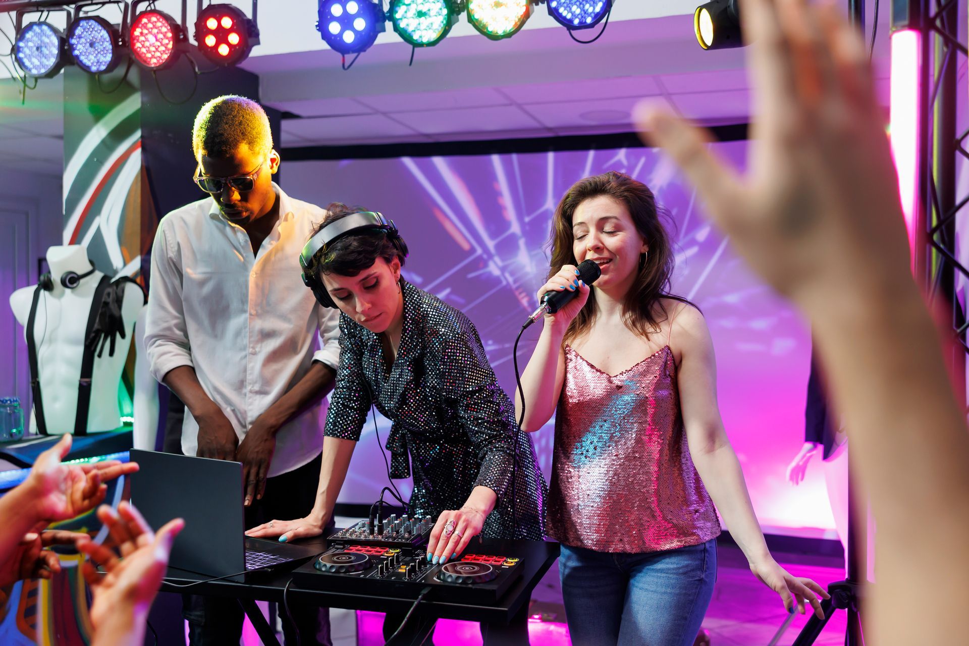 Live music performance with singer at microphone, keyboard player, and colorful stage lights; audience hands raised