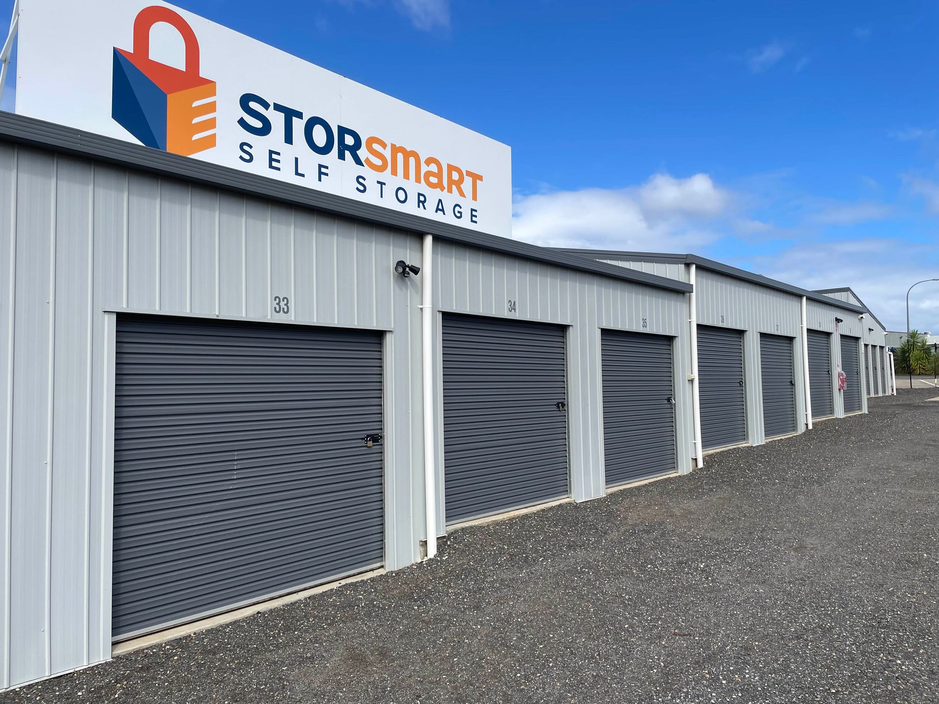 StorSmart Self Storage units with gray roll-up doors and a white metal building under a blue sky
