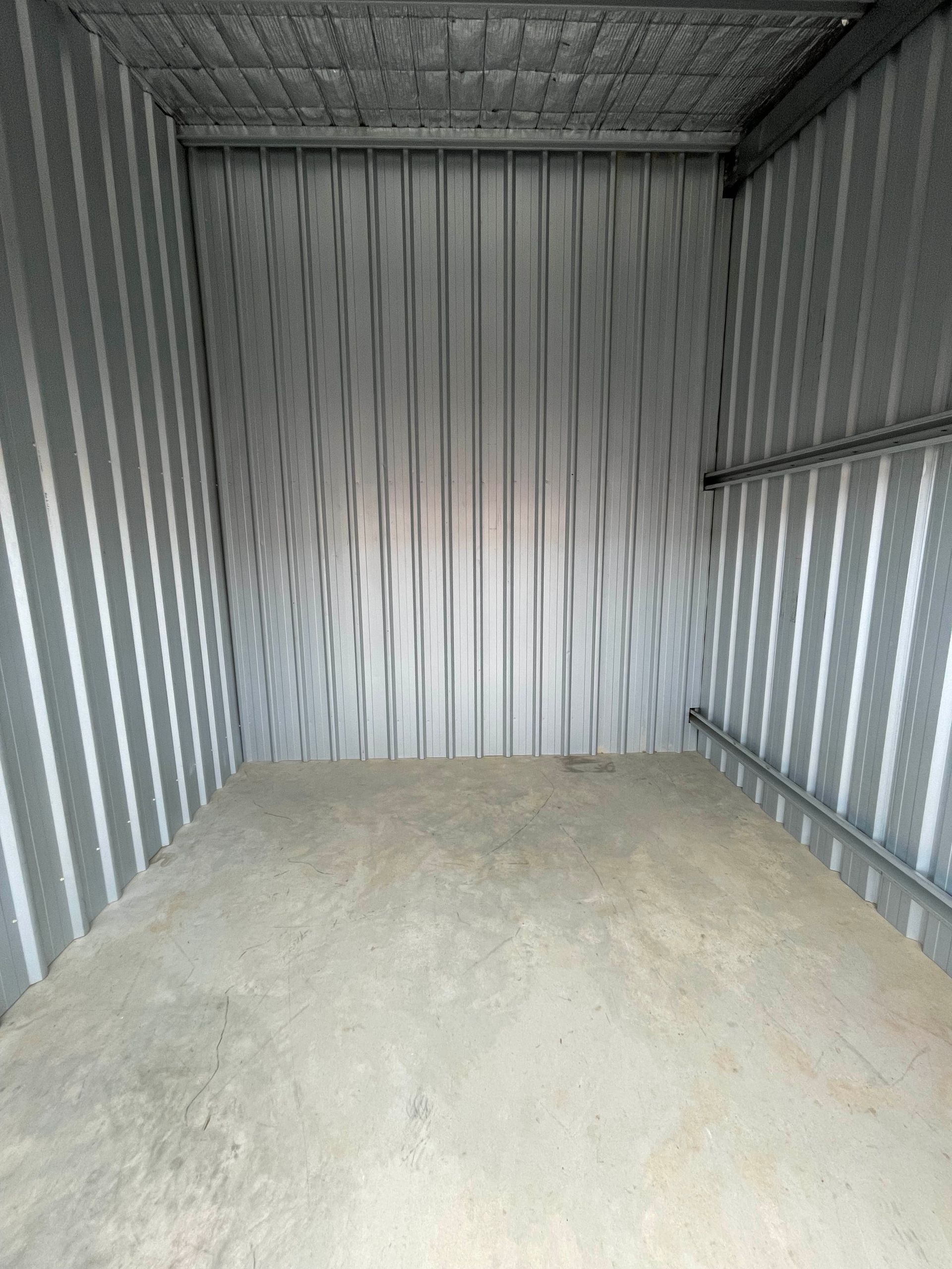 Empty corrugated metal storage unit with a concrete floor and gray interior walls.